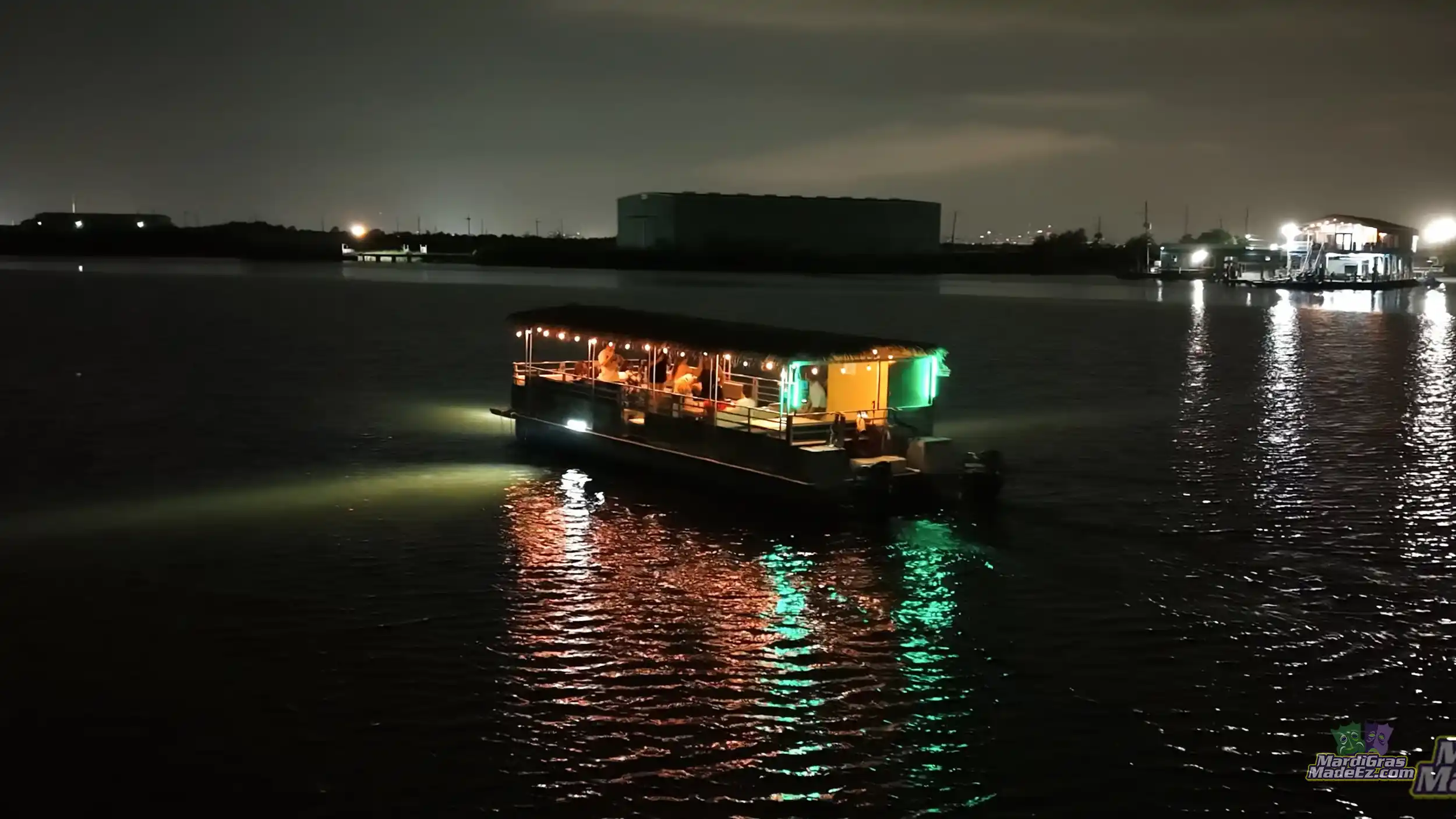 A lit tour boat gliding across dark water at night, its lights reflected on the surface